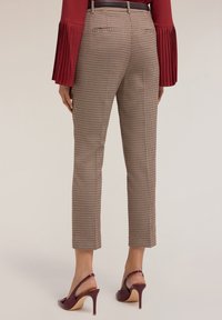 Pantaloni a quadri in tessuto beige e marrone, slim fit, con lunghezza cropped e tasche posteriori, abbinati a tacchi aperti di colore rosso scuro.