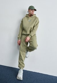 Khaki hættetrøje og joggers i blødt stof, med en frontlomme og logo detalje. Parret med hvide, chunky sneakers.