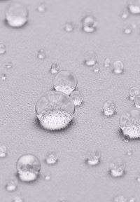 Heldere waterdruppels op gestructureerde grijze stof, variërend in grootte, die licht reflecteren met gladde oppervlakken en ronde vormen.