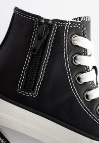 Baskets montantes en cuir noir avec fermeture éclair, lacets blancs, surpiqûres blanches contrastantes et semelle en caoutchouc texturée.