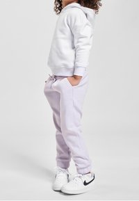 Sweat à capuche blanc associé à un pantalon de survêtement violet clair. Comprend des poignets élastiques, des poches latérales, et des baskets blanches avec des détails noirs.