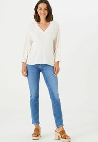 Blusa blanca de cuello en V con mangas abullonadas; combinada con jeans ajustados azules y sandalias de plataforma marrones. Tejido suave con un ajuste relajado.
