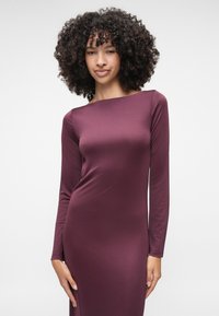 Duga, prilagođena haljina u dubokoj burgundy boji, izrađena od glatkog materijala, s brojnim izrezom i jednostavnim siluetom.