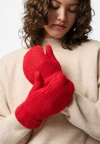 Guanti di lana rossi lavorati a maglia con un motivo a maglia testurizzato e polsini a coste, tenuti insieme di fronte a un maglione beige.