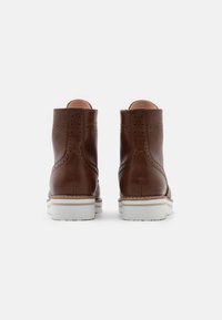 Bottes chevilles en cuir marron avec des perforations, une semelle en caoutchouc blanche et des rayures contrastantes le long de la semelle intermédiaire.