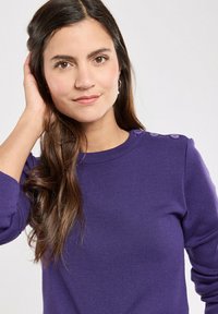 Lila Strickpullover mit langen Ärmeln, gerippten Bündchen und dekorativen Knöpfen an der Schulter. Weiche Textur und taillierte Passform.