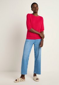 Red knit crewneck sweater with three-quarter sleeves, paired with light blue wide-leg jeans and cream fur-lined sandals.
