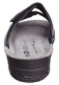 Sort flip-flop med en tekstureret sål, der har en polstret fodseng og et simpelt stropdesign, set fra bagenden.