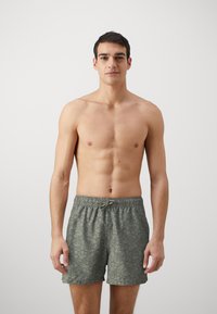 Los pantalones de baño de estampado verde cuentan con una cinturilla elástica con cordón. La tela tiene una textura suave con un diseño de hojas tropicales.