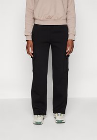 Svarta cargobyxor med två sido fickor, tillverkade av mjukt tyg. Kombinerade med en beige sweatshirt, som har ribbat fåll och muddar.