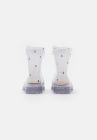 Clear rubber boots with black polka dots, ankle height, textured body, and a translucent sole. No additional hardware or accents.