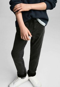 Svarta jeans med smal passform, med dragsko i midjan, detaljerad sömnad och matchade med vita sneakers och en marinblå stickad tröja.