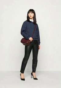 Tumši zili rakstaini džemperis, melni ādas bikses un melnas augstpapēžu kurpes. Bordo krāsas plecu soma, izstādīta pret neitrālu fonu.