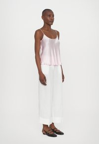 Silk rosa cami med tynne stropper, paret med løse hvite linbukser og svarte flate sko med gullakenter.