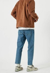 Veste en daim marron, t-shirt blanc, jeans en denim bleu et baskets grises. La veste a une coupe décontractée, les jeans sont fuselés avec une teinte délavée.