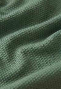 Teksturoidu vihreä kangas, jossa on kennomeri, pehmeä ja sileä pinta, hellästi laskostettu näyttämään sen muokattavuutta ja syvyyttä.