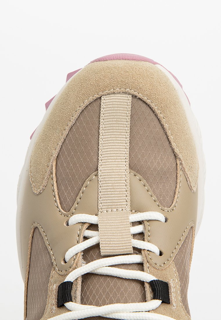 Sneaker beige con materiali in suede e mesh, accenti testurizzati, lacci bianchi e dettagli rosa sul tallone. Presenta un passante sulla linguetta.