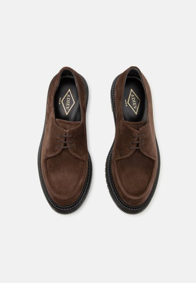 Brown suede shoes with a rounded toe, leather laces, and textured black rubber sole. Interior features logo on a black background.
