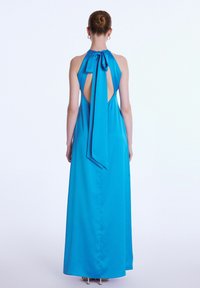 Langes Halterneck-Kleid aus leuchtend blauer Stoff. Es verfügt über einen offenen Rücken mit einer Schleifendetail und fließender Form. Glatte Textur, elegantes Design.