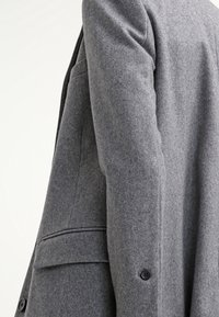 Blazer in misto lana grigia con vestibilità sagomata, revers a punta, chiusura con un bottone e tasche laterali. Finitura testurizzata, dettagli di design minimal.