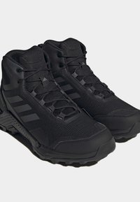 Paire de chaussures de randonnée montantes Adidas Terrex noires avec semelles texturées et fermeture à lacets, montrées sur un fond uni.