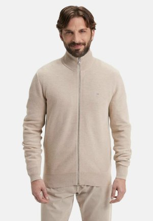 Sweater beige zippé avec un col haut, des manches longues, des poignets et un bas côtelés, fabriqué en matériau tricoté doux, arborant un petit logo.