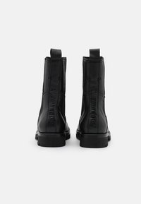 Svarta läderankelboots med en slät yta, med en upphöjd logotypdetalj på baksidan, robust gummisula och dragremmar för enkel påtagning.