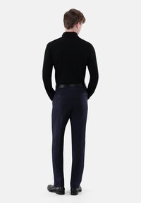 Schwarzes Langarmshirt kombiniert mit marineblauer Hose. Die Hose verfügt über zwei Gesäßtaschen und ist maßgeschneidert mit glatter Textur. Schwarze Schuhe vervollständigen das Outfit.