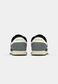 Reebok sportbačiai su juodu viršumi, pilku zomšinės medžiagos kulnu ir kreminių spalvų akcentais. Klasikinis dizainas su plokščiomis raištelėmis ir tekstūruota guma padais.