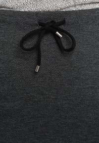 Tissu en denim noir avec une finition texturée, comportant un cordon noir avec des embouts en métal argenté, et une section supérieure à motif contrastant.