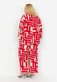 Rød og creme mønstret to-dels outfit med et geometrisk design. Overdelen har en løstsiddende pasform, lange ærmer, og bukserne er bredbenede.