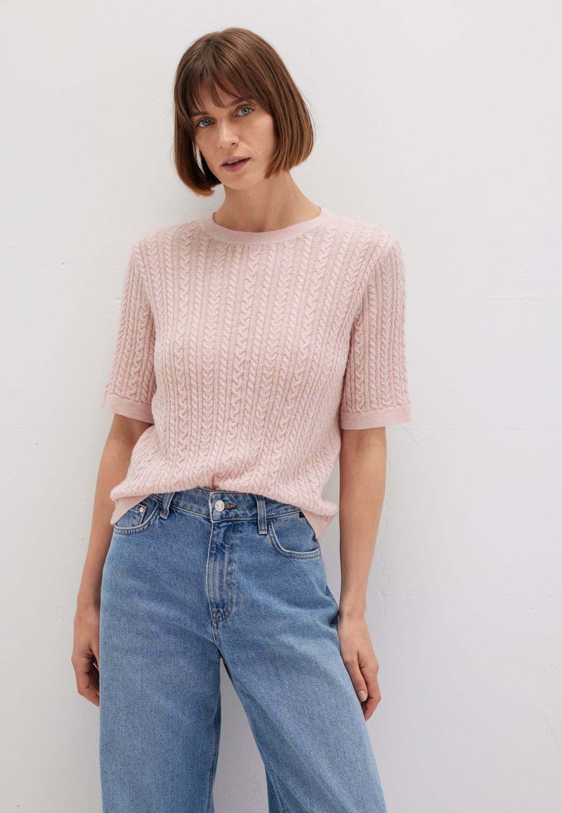 Maglione corto a maniche corte rosa chiaro con un motivo a trecce textured, abbinato a jeans in denim blu chiaro a vita alta.