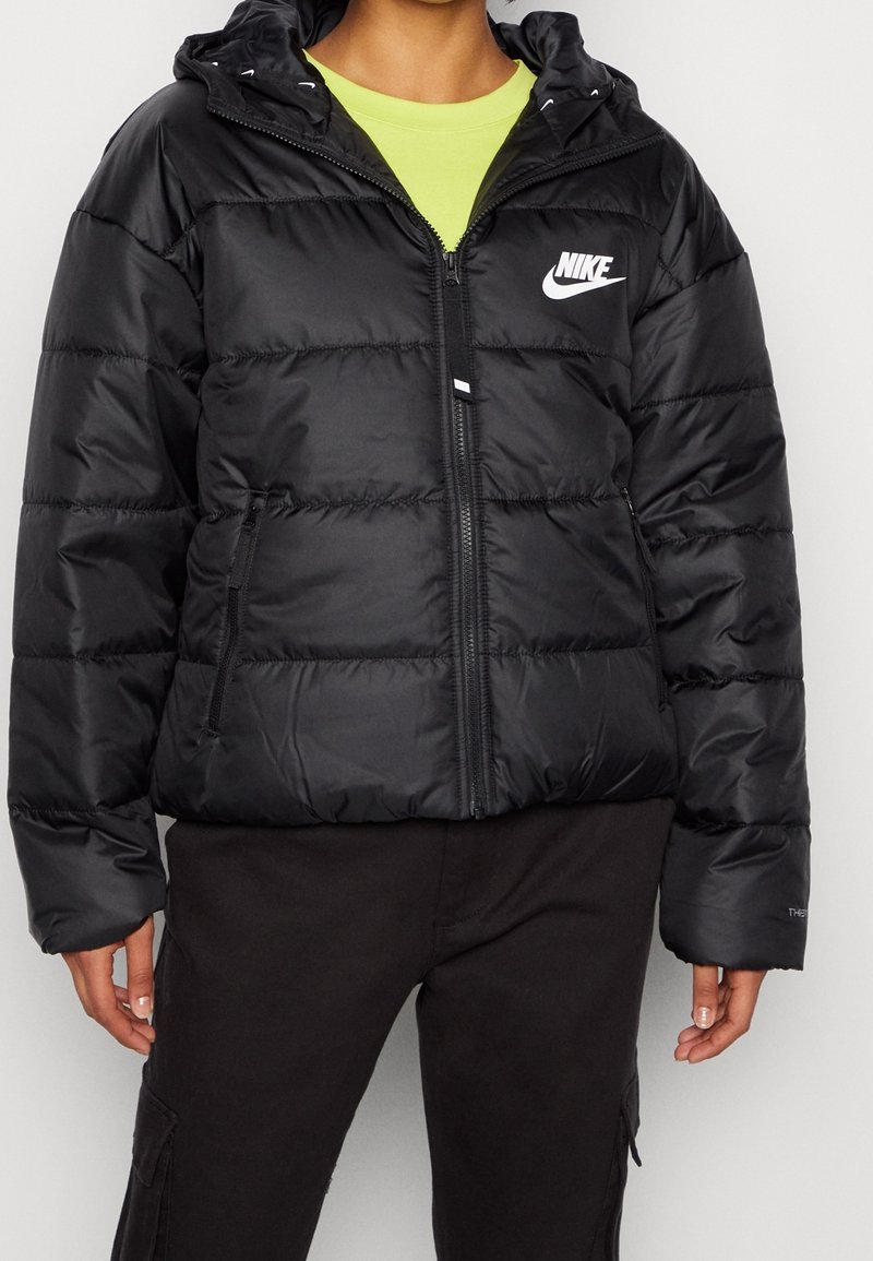 Musta puffatakki, jossa on vetoketjukiinnitys, elastiset hihansuut ja huppu. Vasemmassa rinnassa on valkoinen Nike-logo ja ommellut paneelit.