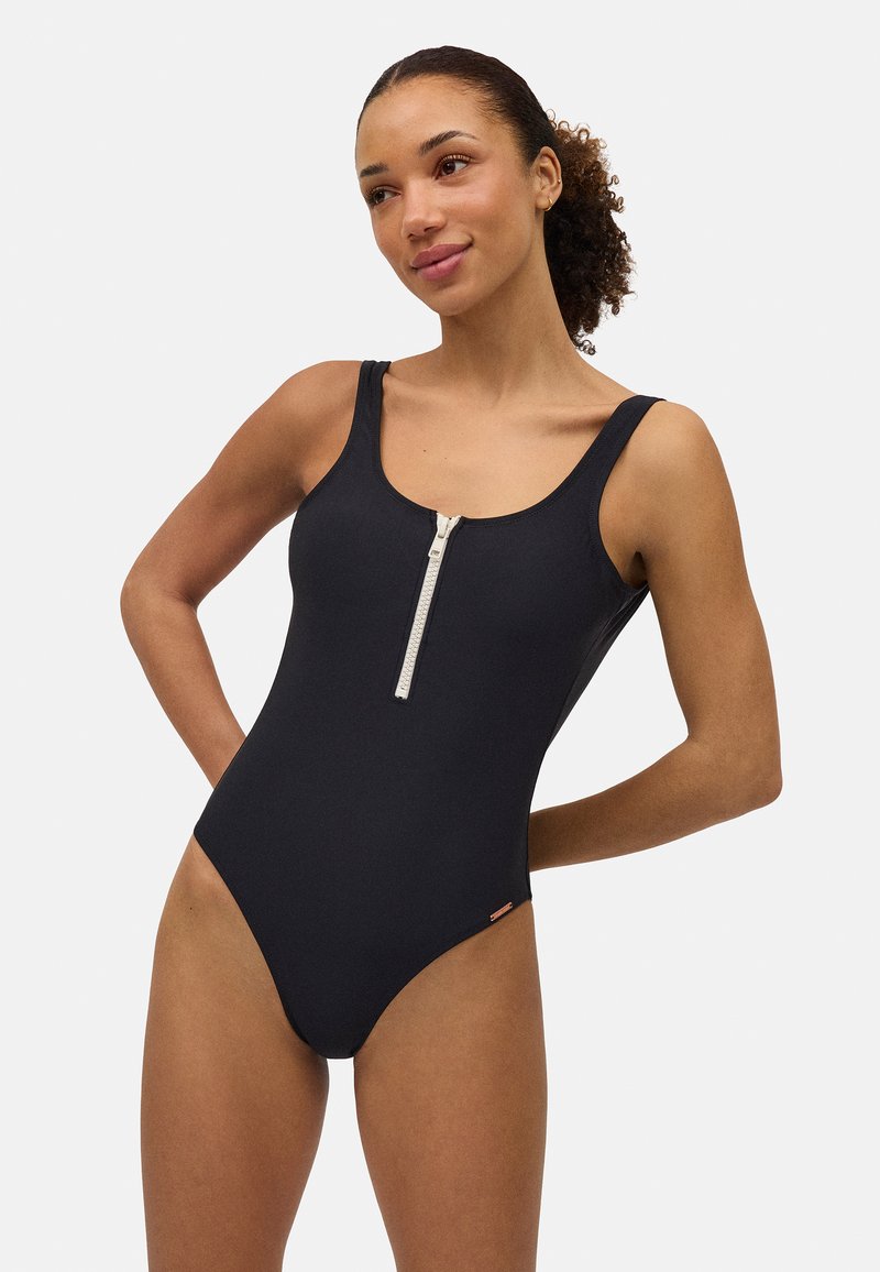 Bañador de una pieza negro con cremallera frontal, tirantes anchos y un diseño ajustado. Hecho de material suave y elástico.