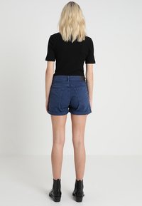 Shorts en denim bleu marine avec une finition texturée, à taille mi-haute et ourlet roulé, dotés de deux poches arrière. Associés à un haut noir.