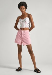 Skraćeni striped top s tankim naramenicama, uparen s pastelno ružičastim trapericama kratkim hlačama s poderanim rubom i istrošenim detaljima, nosi se s crnim sandalama.