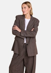 Brun rutete oversized blazer med to frontlommer, sorte knapper og avslappet passform, kombinert med vide bukser i matchende stoff.
