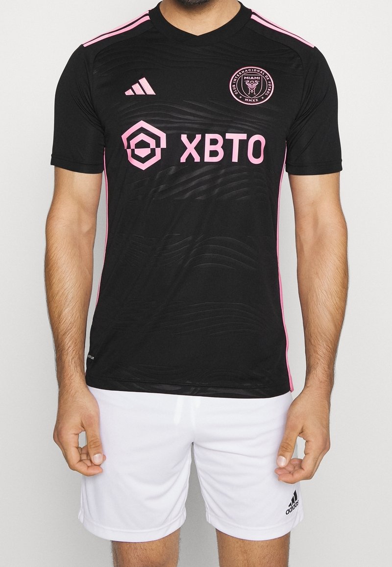 Musta jalkapallopaita, jossa on vaaleanpunaisia yksityiskohtia ja logo, aaltoilevilla kuvioilla ja lyhyillä hihoilla. Yhdistetty valkoisiin shortseihin, hengittävästä materiaalista valmistettu.