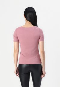 Krátký rukáv, přiléhavý top z jemného fialového materiálu s kulatým výstřihem. Má hladkou texturu, minimální švy a přímý lem.