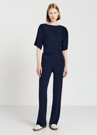 Marineblaues, lässig geschnittenes Oberteil mit kurzen Ärmeln, kombiniert mit passenden weiten Hosen. Beides aus einem weichen Material gefertigt und mit einem minimalistischen Design versehen.