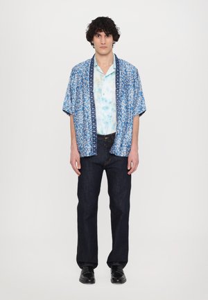 Camicia a maniche corte blu con motivo, con un sotto strato tie-dye, abbinata a jeans scuri in denim e scarpe nere. Fit casual e tessuto leggero.