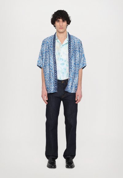 Camicia a maniche corte blu con motivo, con un sotto strato tie-dye, abbinata a jeans scuri in denim e scarpe nere. Fit casual e tessuto leggero.