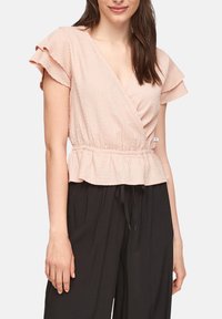 Top de envoltura texturizado en color rosa con mangas rizadas y un dobladillo en peplum, combinado con pantalones negros y fluidos. Cintura con cordón ajustable.