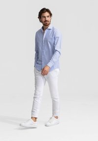 Lichtblauw gestreept overhemd met knopen, witte slim-fit broek en witte sneakers. Het overhemd heeft een klassieke kraag en een getailleerd ontwerp.