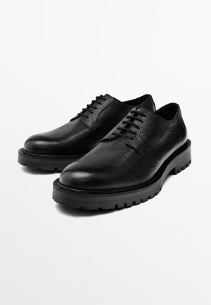 Black leather shoes with textured finish, featuring a rounded toe, flat laces, and a thick rubber sole with traction detailing.