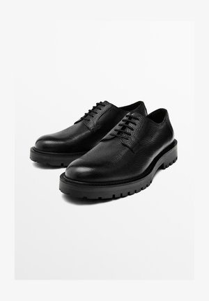 Black leather shoes with textured finish, featuring a rounded toe, flat laces, and a thick rubber sole with traction detailing.