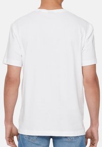 Hvid bomulds t-shirt med korte ærmer, rund hals og en glat tekstur. Vist fra ryggen. Ingen synlig branding eller mønstre.