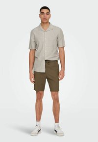 Camisa de botones de manga corta en gris claro combinada con pantalones cortos en verde oliva, que cuentan con una cintura elástica y un corte informal. Se llevan zapatillas blancas.