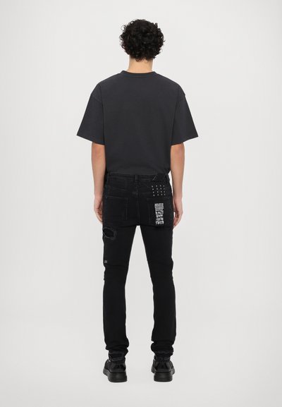 Camiseta negra de gran tamaño y jeans negros desgastados con un parche y tachuelas en el bolsillo trasero. Tejido suave con un ligero brillo.