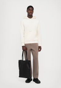 Kremhette med frontlomme, beige bukser og svart totebag. Jevn tekstur; minimalistisk design; mørke sko fullfører antrekket.